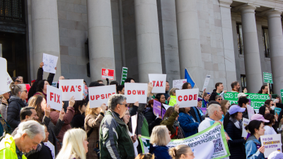 Fuse rally attendees hold signs saying "Fix WA's Upside down Tax Code" on the Capitol steps