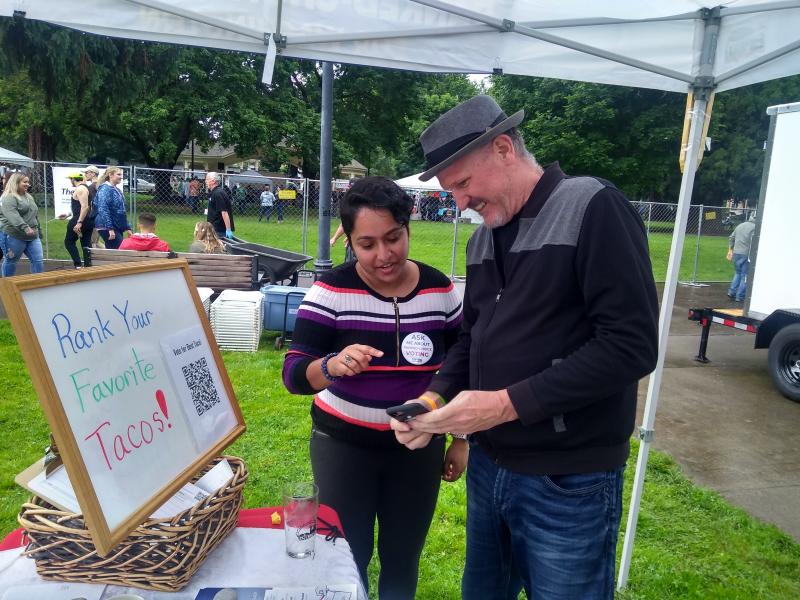 A volunteer explains ranked choice voting to a voter at a community event